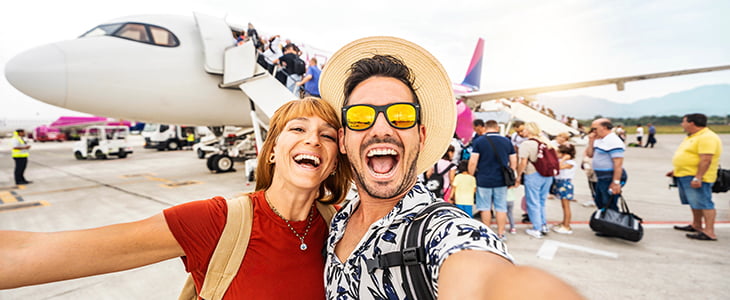 Tourists pose for a photo in front of a loading airplane