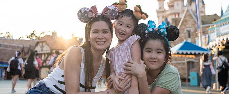 A family wearing mouse ears poses for a photo in front of Disney park