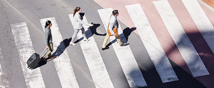 A group of flyers walk on a crosswalk outside an airport