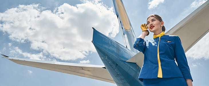 A flight attendant in a uniform stands underneath an airplane