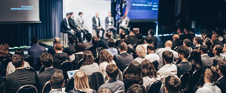 A crowd of convention attendees observe a panel discussion