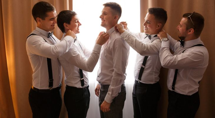 a group of groomsmen help eachother tie ties