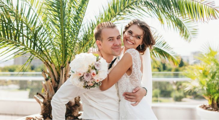 a newlywed couple embrace in front of palm trees