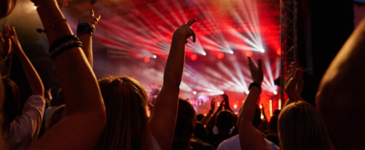 A crowd of concert attendees clap and and dance in front of a stage